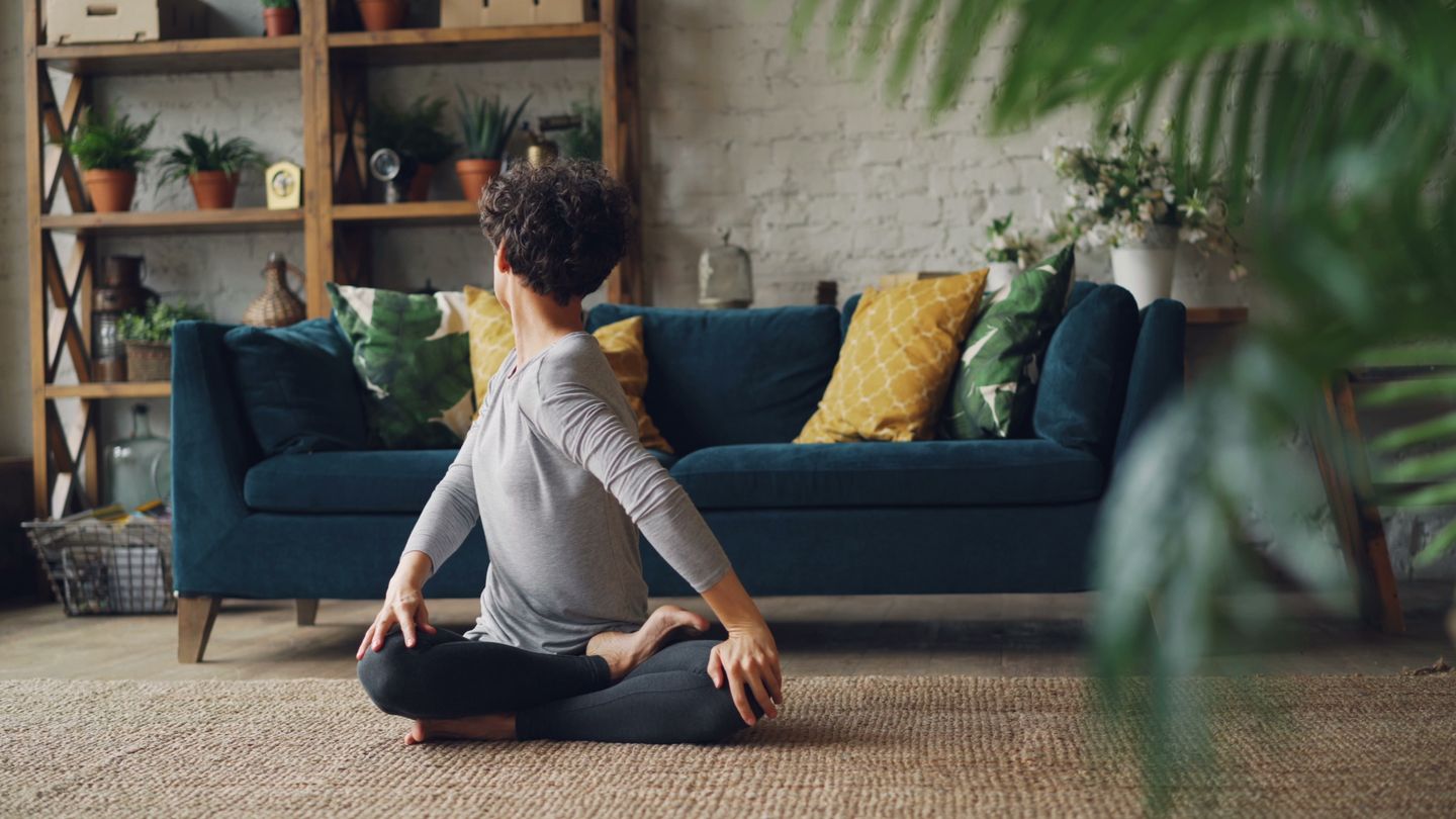 Woman practicing seated yoga in a cozy indoor living room with plants.